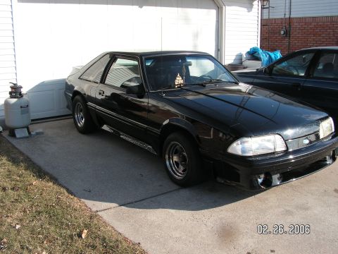 1988 Ford Mustang - A black coupe is parked in front of a garage door, with another vehicle visible to the right.