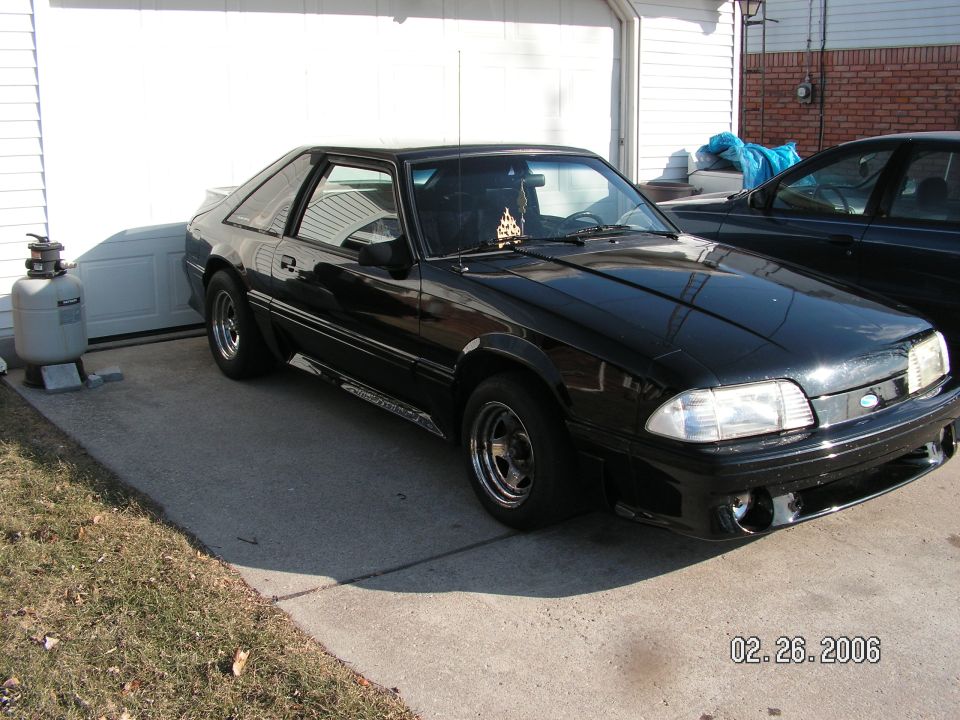 Black coupe parked on concrete driveway, front 3/4 view