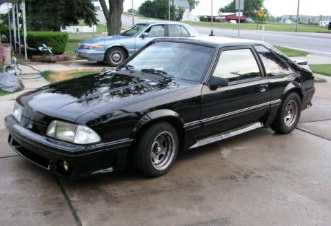 1988 Ford Mustang - A black 1988 Ford Mustang is parked in front of a house, with another car visible in the background.