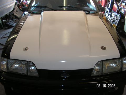 1988 Ford Mustang - The front of a car is shown, a prominent white hood scoop and black fenders with hood pins.