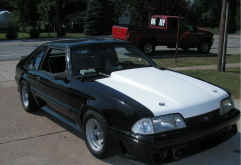 1988 Ford Mustang - A black and white Ford Mustang is parked outside, with a red pickup truck in the background.