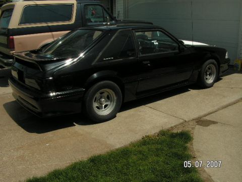 1988 Ford Mustang - A black coupe is parked on a concrete driveway with a tan SUV behind it.