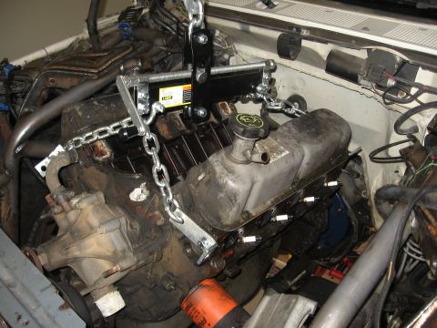 1990 Ford Bronco - greasy V8 engine and transmission suspended by an engine-lift chain over an open engine bay during a swap.