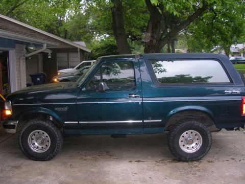 1994 Ford Bronco - A dark green Ford Bronco is parked in a driveway next to a house.