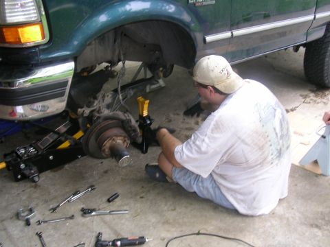 1994 Ford Bronco - A man works on the front suspension of a green Ford truck, which appears to be from the early 1990s.