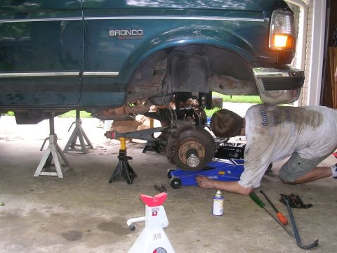 1994 Ford Bronco - A mechanic works on the suspension of a 1994 Ford Bronco lifted on jack stands.