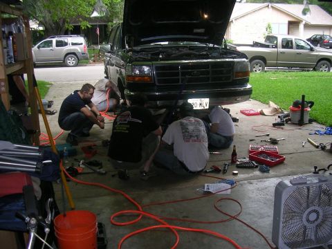 1994 Ford Bronco - A group of people are gathered around a 1994 Ford Bronco, performing maintenance in a driveway setting.