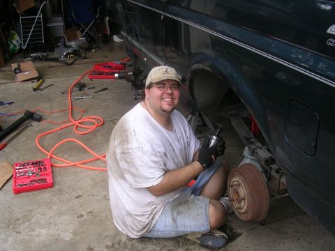 1994 Ford Bronco - A man works on the rear wheel of a dark green SUV, with tools and parts visible on the garage floor.