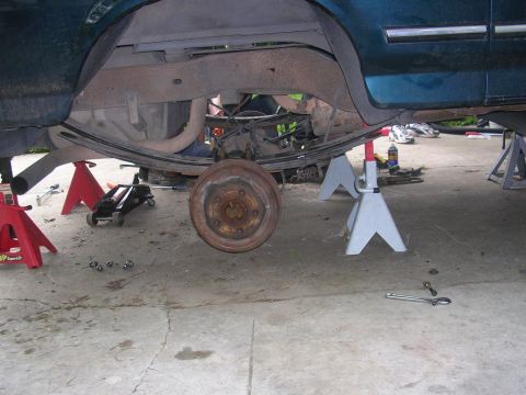 1994 Ford Bronco - Vehicle's rear axle and leaf springs are visible while it is raised on jack stands for maintenance.