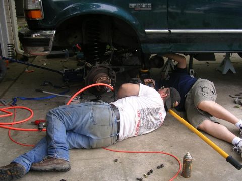 1994 Ford Bronco - Mechanics perform maintenance on a 1994 Ford Bronco, lifting it for access to the suspension and drivetrain.