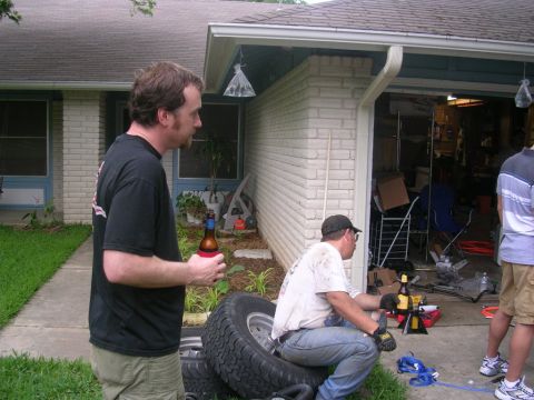 1994 Ford Bronco - Men gather around tires and a garage entrance, with one man holding a beer.
