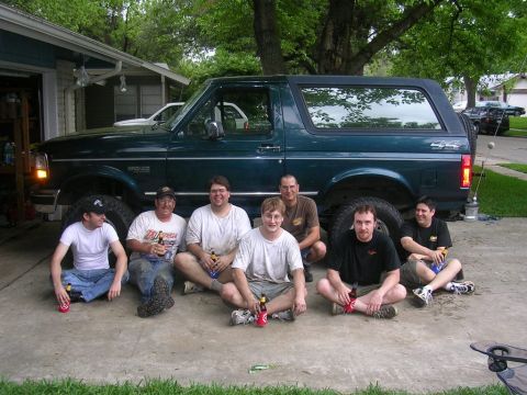 1994 Ford Bronco - Seven men are gathered around a dark green Ford Bronco parked in a driveway.