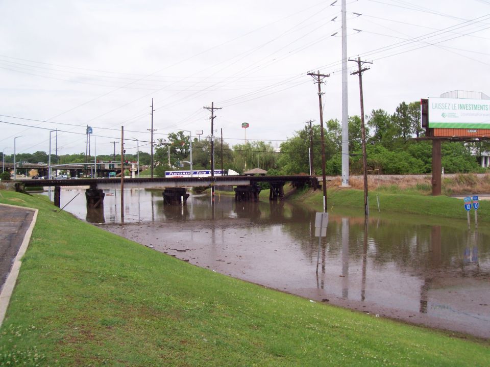 Flooded road with a bridge over murky water. Power lines and a billboard are visible