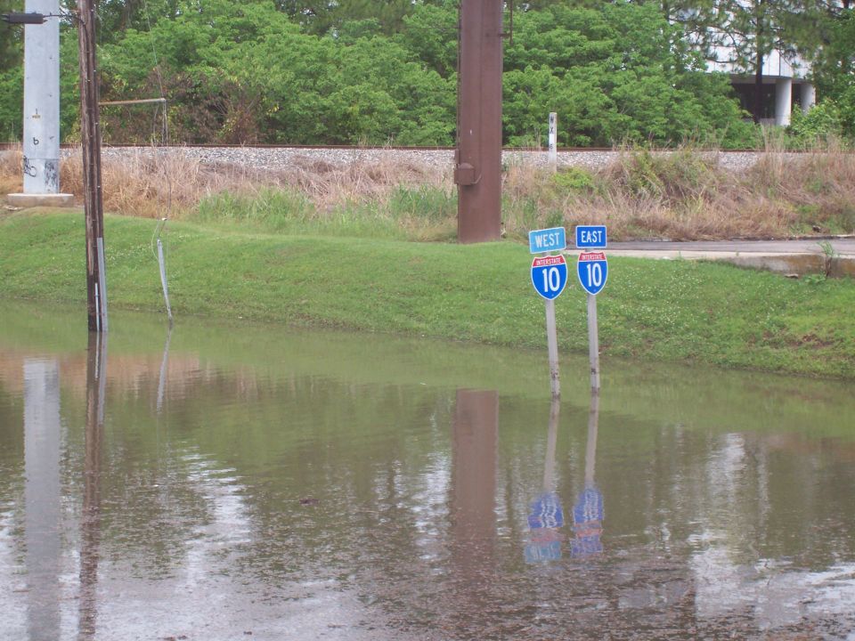 Flooded road with two highway signs for I-10 West and East