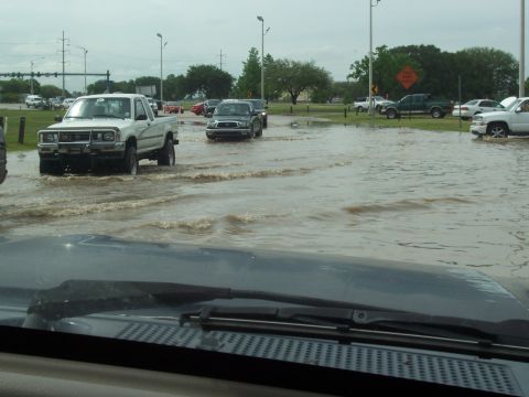 1992 Ford Bronco - Vehicles navigate through deep floodwaters on a street with traffic lights and trees in the background.