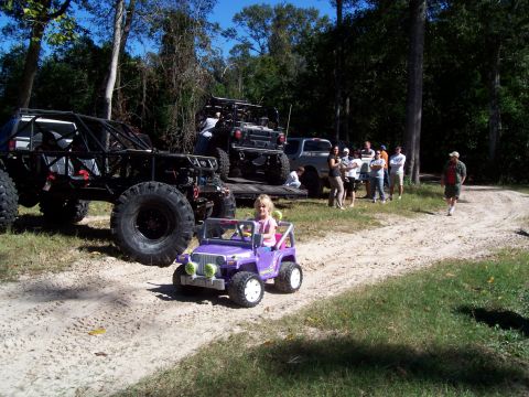 1992 Ford Bronco - A group of people and off-road vehicles are gathered on a dirt path in a wooded area.