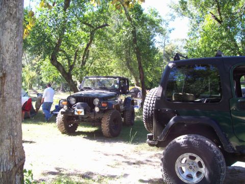 1992 Ford Bronco - Two Jeeps are parked in a wooded area, with tents and people visible in the background.