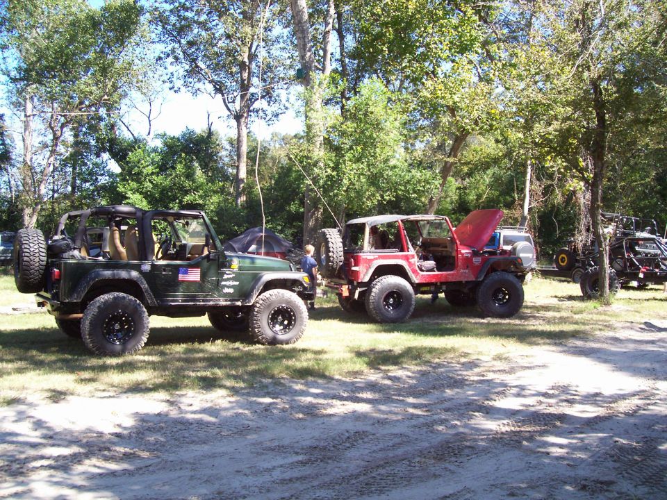 Two Jeeps, one green and one red, parked on a dirt path with trees in the background