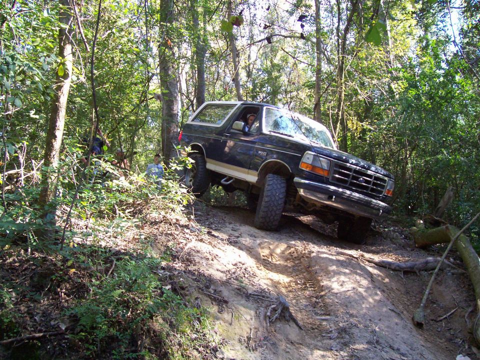 Dark blue 1992 Ford Bronco with a white top, angled on a dirt trail with trees