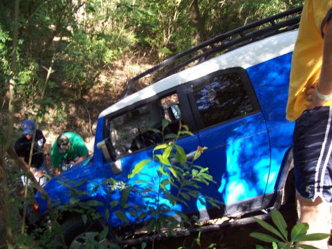 1992 Ford Bronco - A blue and white SUV navigates a wooded trail, with people attending to it.
