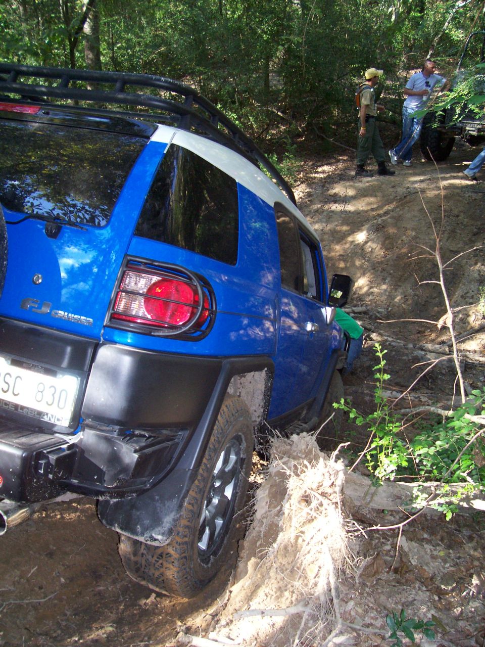 Blue Toyota FJ Cruiser stuck in mud on a wooded trail with people watching