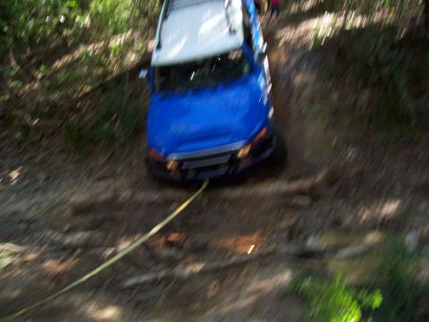 1992 Ford Bronco - A blue SUV navigates a muddy trail, its front end angled downwards as it's pulled by a rope.