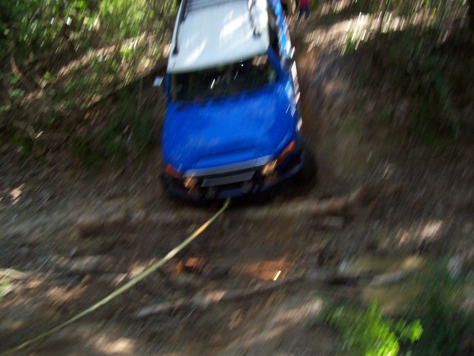 Blue SUV with white roof on a dirt path, being pulled by a yellow rope