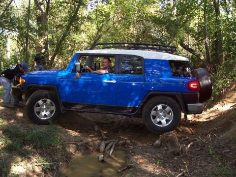 1992 Ford Bronco - This blue and white SUV is shown off-roading through a wooded area, with a spare tire mounted on the rear.