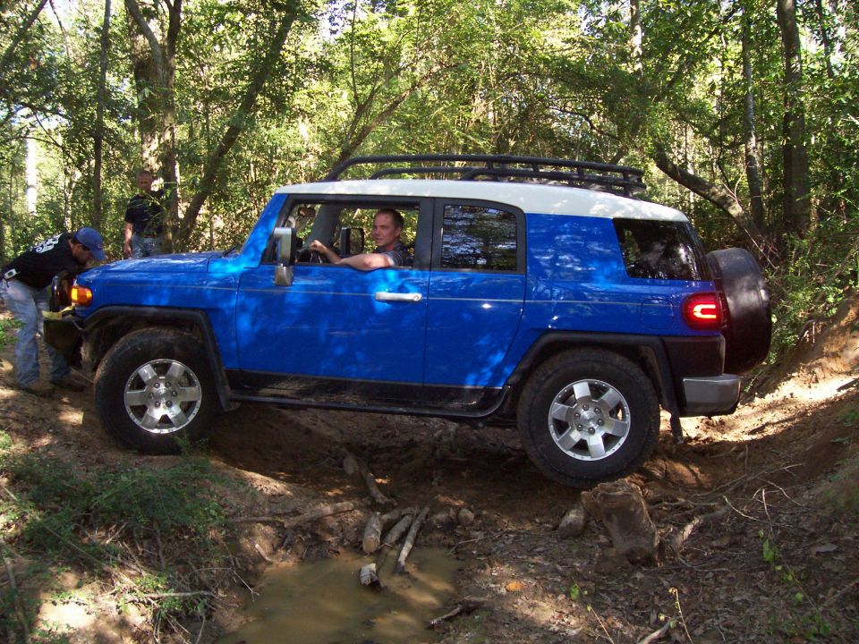 Blue and white SUV navigating rough terrain with a spare tire on the back