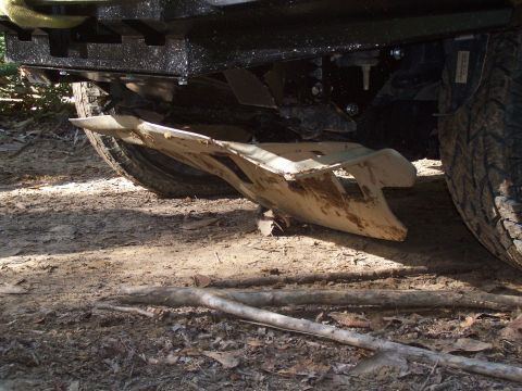 1992 Ford Bronco - Close-up of an off-road vehicle's skid plate and tire on a dirt path.
