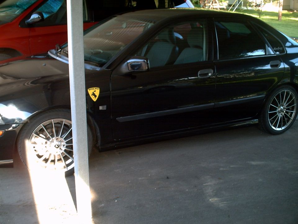 Black sedan with Lamborghini emblem and chrome multi-spoke wheels under carport