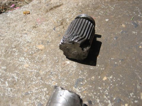 1990 Ford Bronco - A close-up of a damaged metal component, likely a driveshaft or axle, resting on concrete.