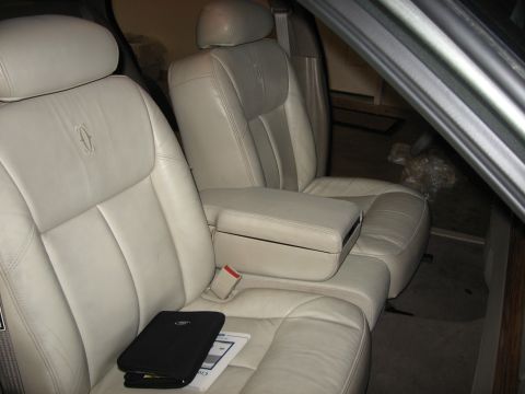 2001 Ford Crown Victoria - The interior of a car shows cream leather seats and a center console, with a black case and manual on the passenger seat.