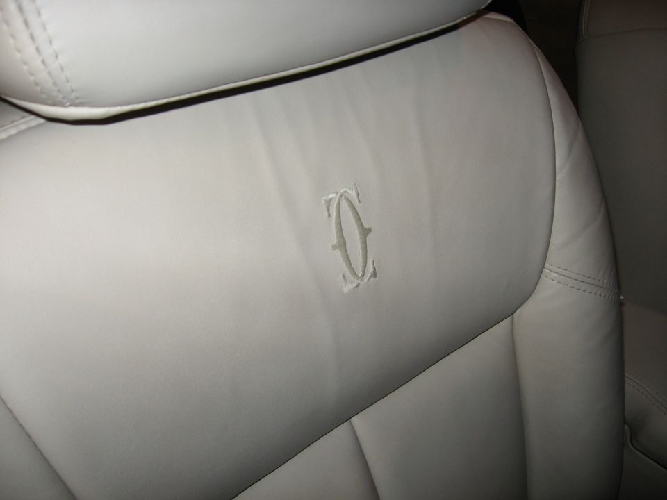 Close-up of a light-colored leather car seat with an embossed logo in the center