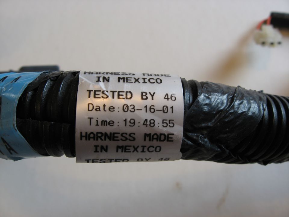 Close-up of a black automotive wiring harness with a label showing it was made in Mexico and tested on 03-16-01