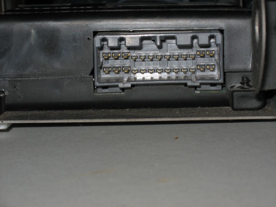 Gold-pin multi-pin connector on back of black automotive electronic module, pins numbered 26 and 14