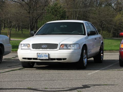 2003 Ford Crown Victoria - A white Ford Crown Victoria is parked in a lot, with other vehicles nearby. The front of the car is visible.