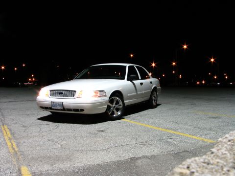 2003 Ford Crown Victoria - A white 2003 Ford Crown Victoria is parked in a lot at night, illuminated by streetlights.