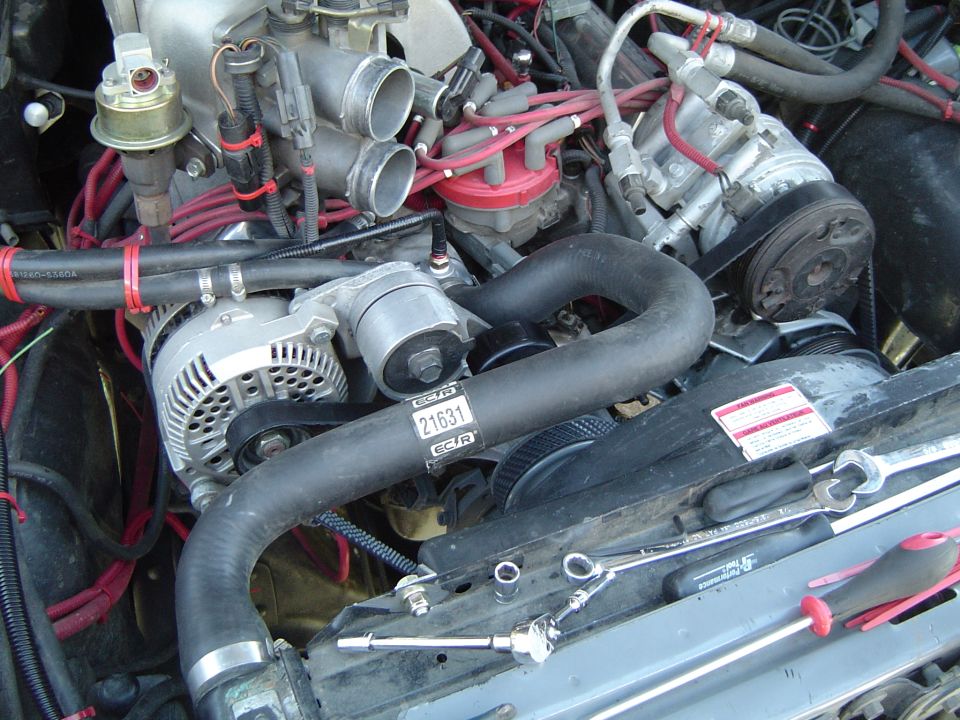Engine bay of fuel-injected V8 with red plug wires, alternator, A/C compressor and tools on radiator support