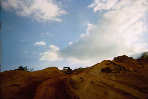 1990 Ford Bronco - An off-road vehicle navigates a steep dirt incline under a dynamic sky with scattered clouds.