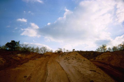 1990 Ford Bronco - Off-road vehicles navigate sandy terrain under a partly cloudy sky.