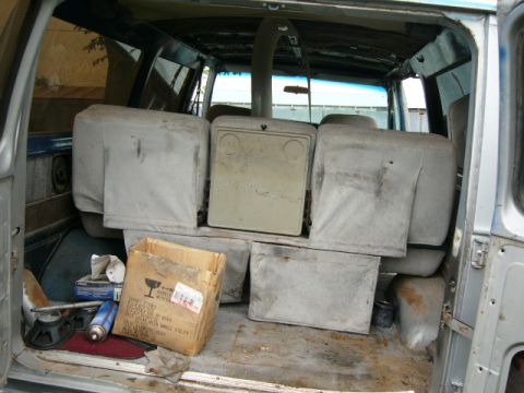 1978 Ford E250 - The rear interior of a van is filled with seats and miscellaneous items, including a cardboard box and spray cans.