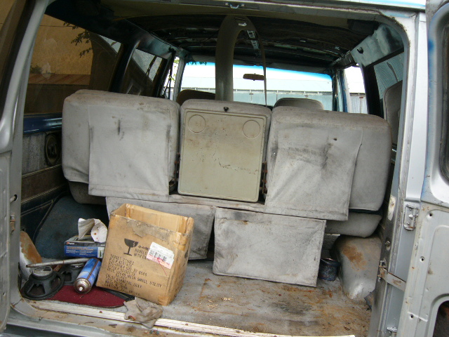 Interior of a van showing rows of seats, a cardboard box, and various items on the floor