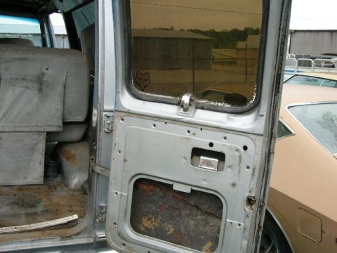 1978 Ford E250 - Interior view of a van door, revealing worn seats and a bare metal panel, with another vehicle visible outside.