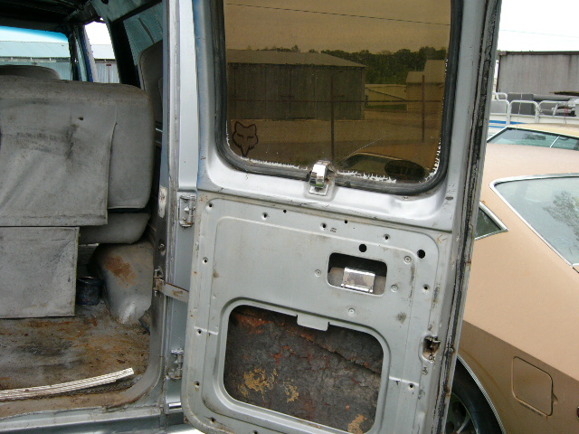 Open van door interior showing grey seats, rusted floor, and bare metal door panel with a Fox logo sticker on the window