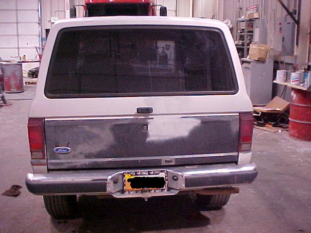 Rear view of a two-tone Ford Bronco II with a dark gray tailgate and chrome bumper