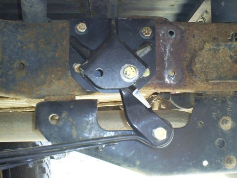 1994 Ford F-250 - A black metal suspension part is attached to the rusty frame of a vehicle.