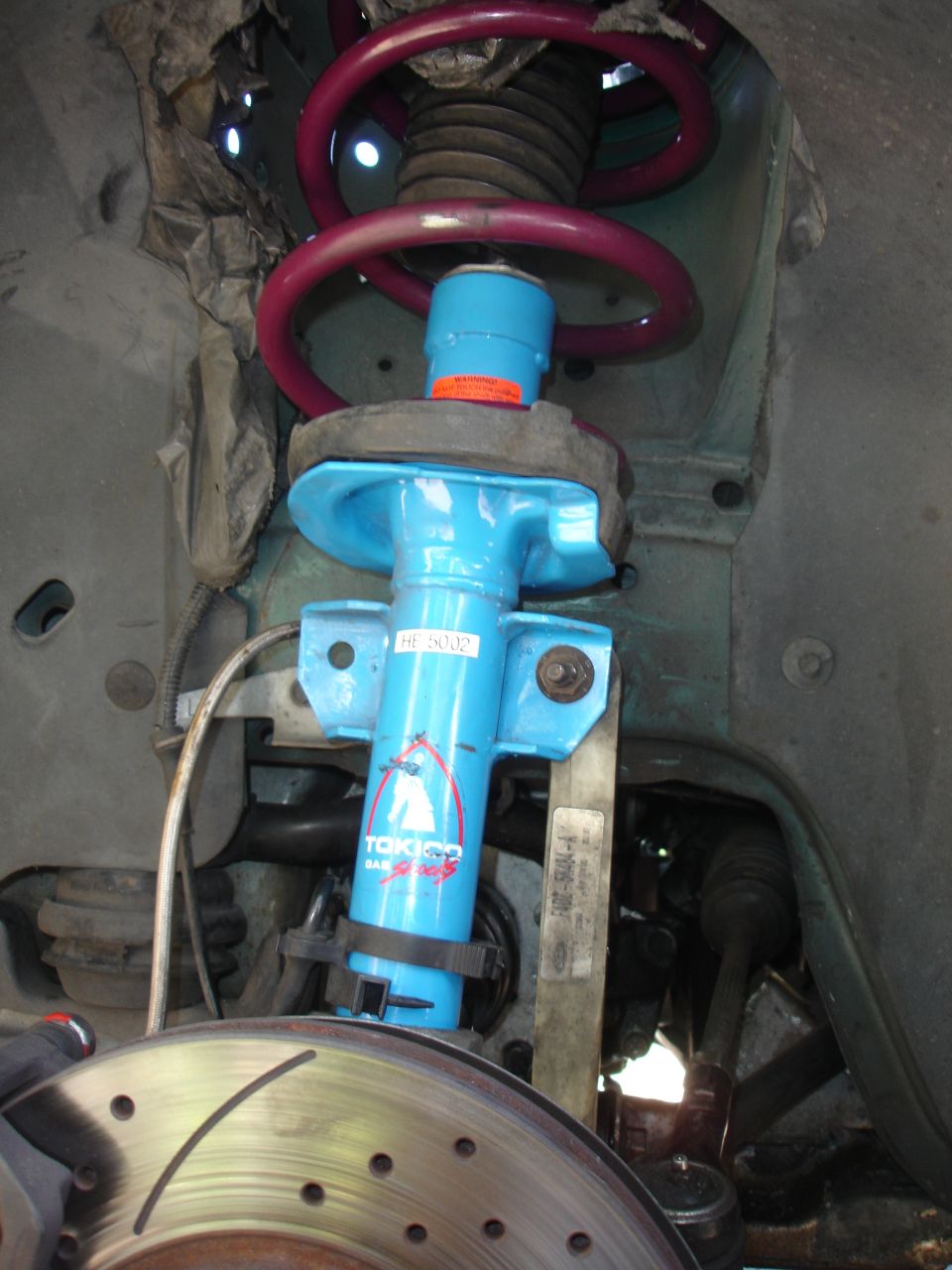 Blue Tokico shock absorber with red coilover spring and slotted brake rotor