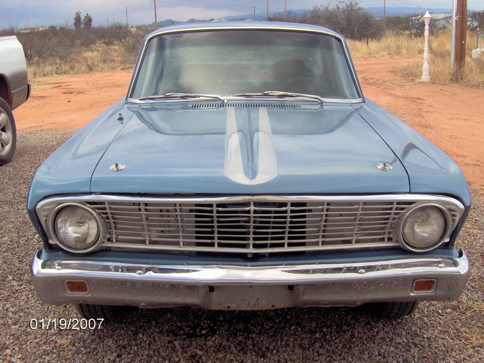 Front view of a light blue classic car with a silver stripe on the hood. It has a chrome grille and headlights