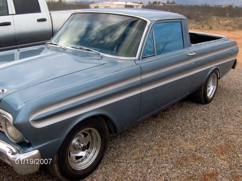 1964 Ford Ranchero - A blue 1964 Ford Ranchero pickup truck is seen from a three-quarter front angle, parked next to a silver pickup truck.